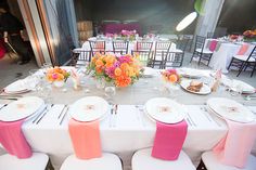 the table is set with white and pink linens, silverware, and flowers