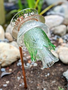 a glass bird feeder sitting on top of a rock covered ground