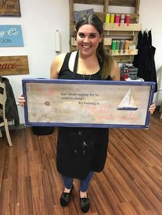 a woman holding up a framed sign with a sailboat on it's side