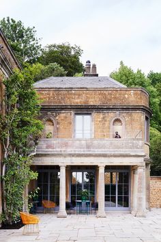 an old brick building with two chairs and tables in front of it, surrounded by greenery