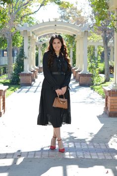 a woman is standing on the sidewalk with her hand in her pocket and wearing a black dress