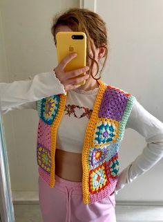 a woman taking a selfie in front of a mirror wearing a colorful crocheted vest