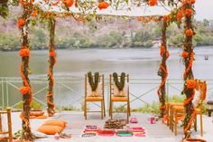 an outdoor ceremony setup with orange flowers and greenery on the ground, overlooking a lake