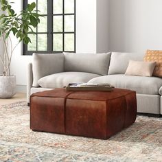 a living room with a couch, ottoman and coffee table in front of a window