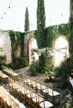 an outdoor ceremony set up with gold chairs and white tablecloths, surrounded by greenery