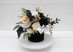 a white and black flower arrangement in a black vase on a white pedestal with wood planks