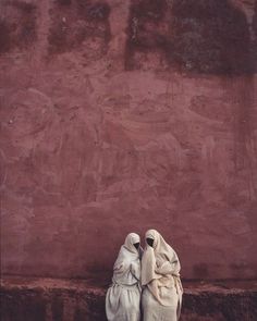 two white statues sitting against a red wall