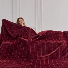 a woman hiding behind a red blanket on top of a white wall with her hands in the air