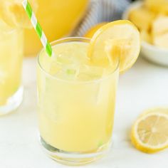 two glasses filled with lemonade sitting on top of a table next to sliced lemons