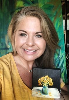 a woman holding up a painting with flowers in it