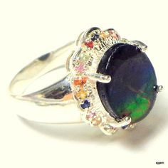 This Awesome Gemstone is a Rare find. It is called Ammolite, and was a fairly recent discovery, found in the depths of the earth in Canada. This is a 10mm x 14mm, oval shaped triplet, set in an Awesome Sterling Silver Ring Setting, with multi-colored, Fancy Sapphire accents. This Beautiful stone, discovered by accident, around 25 years ago, is the petrified shell of a million year old snail. Coveted by collectors, this stone has a glowing property, the likes of which has never been seen until it Multicolor Cabochon Gemstones For Fine Jewelry, Multicolor Cabochon Gemstones Fine Jewelry, Fine Jewelry Multicolor Cabochon Gemstones, Multicolor Cabochon Rings For Formal Occasions, Formal Multicolor Cabochon Rings, Multicolor Oval Gemstones For Anniversary, Oval Multicolor Gemstones For Anniversary, Multicolor Multi-stone Opal Ring, Multicolor Gemstones For Formal Occasions