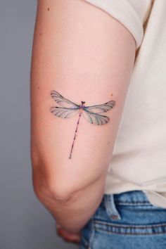 a woman's arm with a small dragonfly tattoo on the back of her left arm