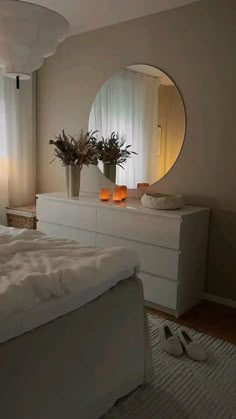 a bedroom with a bed, dresser and large round mirror on the wall above it