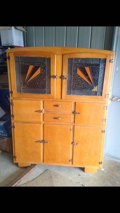 an old wooden cabinet with two doors and some glass panels on the front, sitting in a garage