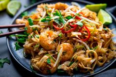 a plate filled with noodles and vegetables next to chopsticks on a table top