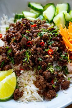 a white plate topped with rice, meat and veggies next to sliced cucumbers