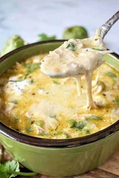 a spoon full of cheese and broccoli being lifted from a green casserole dish