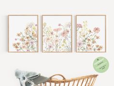 three floral paintings hanging on the wall next to a wicker basket with a blanket