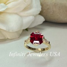 a close up of a ring with a red stone on it and flowers in the background