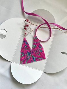 a pair of pink and blue beaded earrings on top of a piece of paper