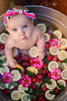 a baby is sitting in a pot full of lemons and strawberries with a bow on her head