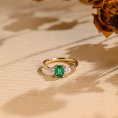 an emerald and diamond ring sits next to a flower