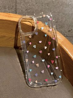 an iphone case with hearts on it sitting on a leather chair next to a wooden arm