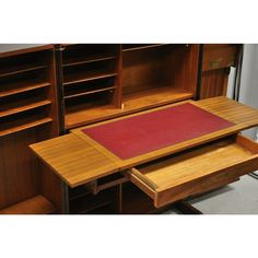 a wooden desk with two drawers and a red rug on it's top, in front of some bookshelves