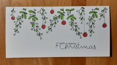 a christmas card with holly and berries hanging from it's sides on a wooden surface