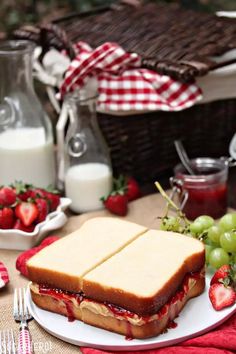 a sandwich on a plate with strawberries next to milk and fruit in the background