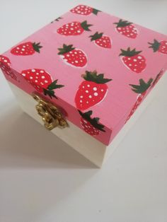 a pink box with strawberries painted on the side and gold handles sitting on a white surface