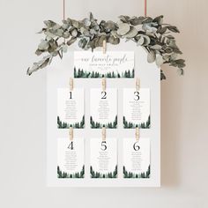 a wedding seating chart hanging on a wall with eucalyptus leaves and greenery around it