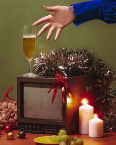 a hand reaching for a glass of wine in front of a television set with christmas decorations and candles