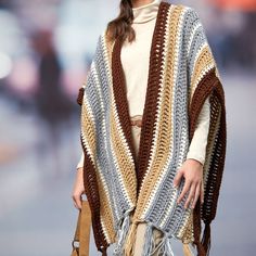 a woman is walking down the street wearing a crocheted ponchy and holding a purse