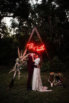 a bride and groom kissing in front of a neon sign