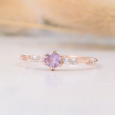 a pink sapphire and diamond ring sitting on top of a white surface with feathers in the background