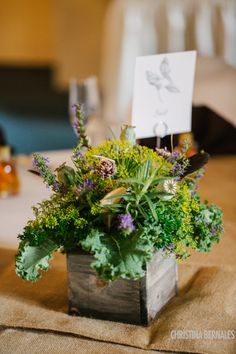 an arrangement of flowers and greenery in a wooden box on a table with place cards