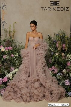 a woman standing in front of flowers wearing a dress with ruffles on it