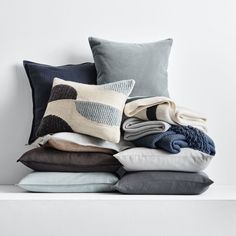 a pile of pillows and blankets on top of a white shelf next to each other