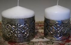 two white candles sitting next to each other on top of a red and gold table cloth