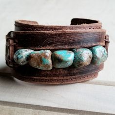 Distressed Finish Leather Cuff features a genuine strand of chunky African Turquoise. Each strand is different and will show varying shades of the natural stone. ***Please view all the pictures as they show examples of the many stone colors Cuff measures 2" by 9" in length Adjustable to 7" and 7.5" Although your item will resemble the photo, each piece is created by hand, so no two are identical.Thank you for visiting The Jewelry Junkie! Adjustable Turquoise Cuff Bracelet With Natural Stones, Adjustable Turquoise Leather Bracelet In Rustic Style, Adjustable Rustic Turquoise Leather Bracelet, Southwestern Adjustable Cuff Bracelet With Natural Stones, Rustic Handmade Turquoise Cuff Bracelet, Bohemian Turquoise Cuff Bracelet With Patina, Turquoise Bohemian Cuff Bracelet With Patina, African Turquoise, Wide Cuff