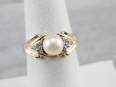 This vintage pearl ring has a sleek chevron design crafted from yellow gold. The polished gold frames the pearl beautifully, which has a gorgeous creamy white luster with hints of gray undertones. This single pearl is accented by a trio of sparkling diamonds making this the perfect piece to gift for a variety of occasions! Metal: 14K Yellow Gold Gem: Pearl Gem Measurements: 6.7 mm, Round Accents: 6 Diamonds totaling .04 Carats, H in Color, I1 in Clarity Ring Size: 6.50 Marks: "14K A" Stamped on Classic White Pearl Ring With Diamond Accents, Classic Pearl White Diamond Ring, Classic Pearl White Diamond Ring For Formal Occasions, Classic Akoya Pearl Rings With Diamond Accents, Classic Pearl Rings In Diamond White, Classic Diamond Pearl Ring In Pearl White, Classic Pearl Diamond Ring With Accents, Classic Diamond Pearl Ring In White, Classic Pearl Diamond Ring With Diamond Accents