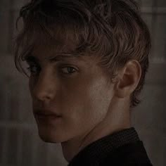 a young man is staring at the camera in a dark room with light coming from behind him