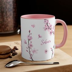 a pink and white coffee mug sitting on top of a wooden table next to a cookie