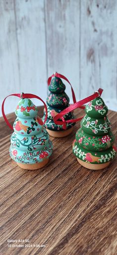 three small ceramic christmas trees on top of a wooden table with red ribbon tied around them