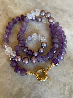 "Jammy shades of purple including Amethyst gemstones, Pearl and, Natural Quartz have been hand knotted on silk to create this one of a kind ombre necklace. A \"sailor\" bolt clasp in 24 karat gold overlay allows charms and pendants to be swapped on and off with ease. Wonderful to wear alone, layered or styled with your favorite medals and charms. The necklace measures approximately 20\" inches end to end and, the gemstones are approximately 8mm. Some stretching will naturally occur with knotted Purple Gemstones, Ombre Necklace, Candy Necklace, Silk Jewelry, Candy Necklaces, Stackable Bangles, Necklace Purple, Gold Overlay, Stacked Bangles