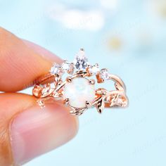 a woman's hand holding a ring with an opal and leaves design on it