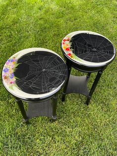 two black tables with spider web designs on them sitting in the middle of some grass