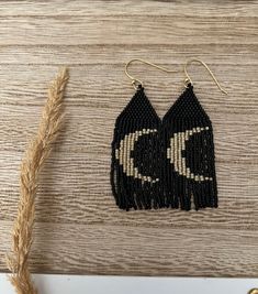 the black and white beaded earrings are hanging from gold earwires on a wooden surface