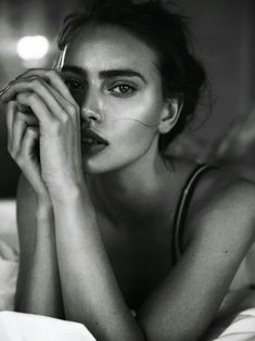 a black and white photo of a woman laying in bed with her hands on her face